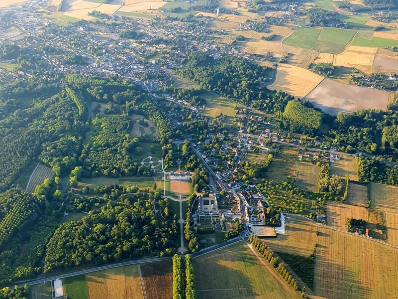 Montgolfière colorée survolant un château entouré de verdure et d'un lac