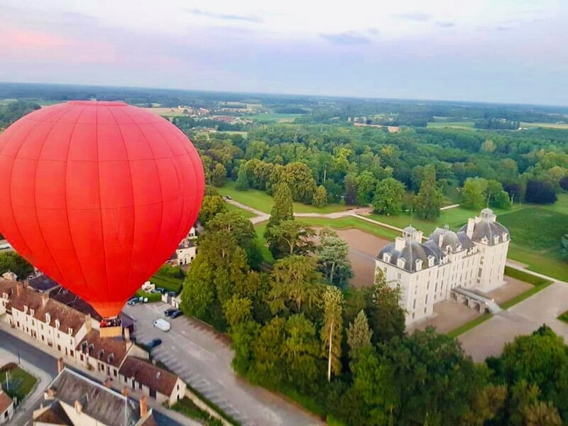 Montgolfière colorée survolant un château entouré de verdure et d'un lac