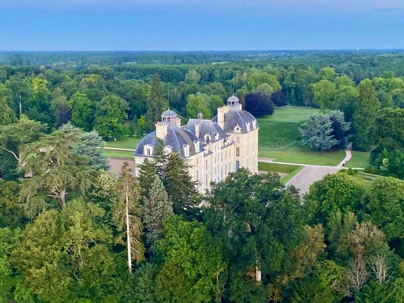Montgolfière colorée survolant un château entouré de verdure et d'un lac