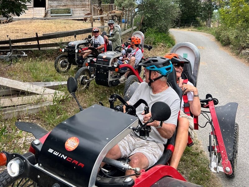 Quatre personnes sur des véhicules tout-terrain rouges et noirs sur une route goudronnée près d'une clôture en bois.