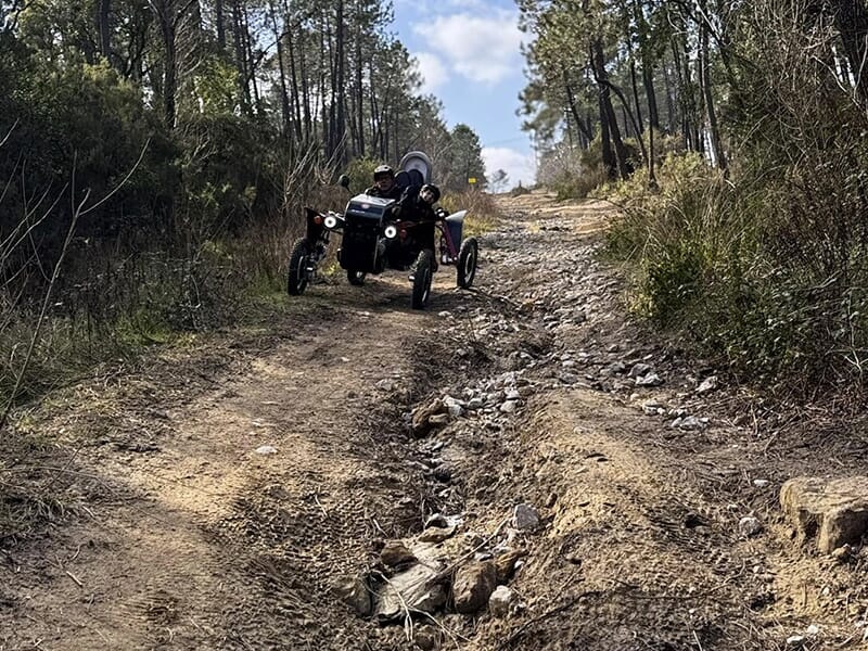 Véhicule tout-terrain électrique roulant sur un sentier accidenté dans une forêt, avec deux personnes à bord.