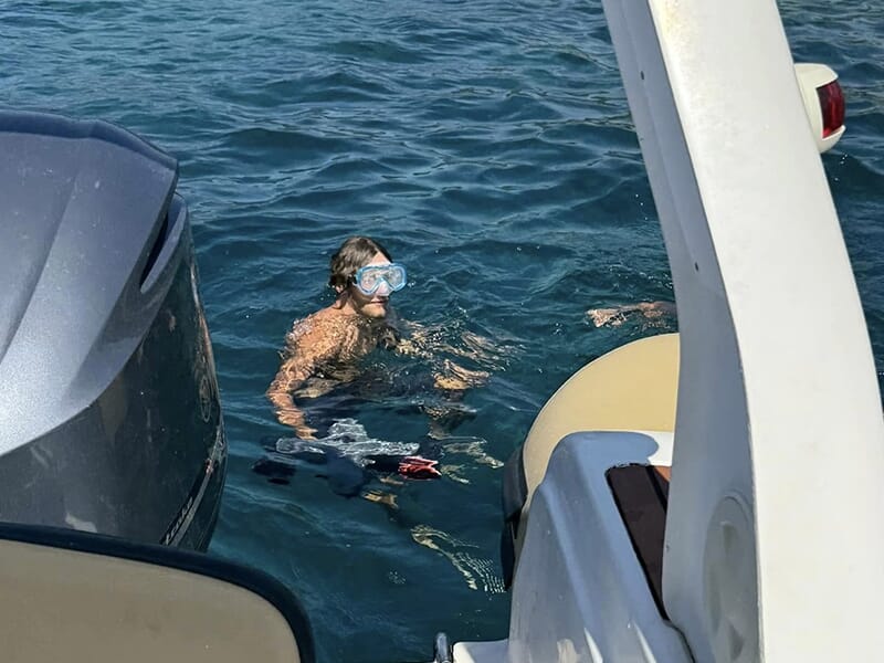 Homme avec masque et tuba dans l’eau près d’un bateau, prêt à faire du snorkeling.