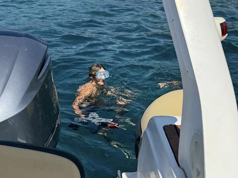 Homme avec masque et tuba dans l’eau près d’un bateau, prêt à faire du snorkeling.