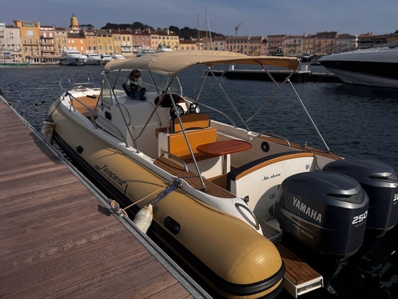 Bateau pneumatique Tempest amarré au port, équipé de deux moteurs Yamaha 250, avec un enfant assis à l'avant, fond de maisons colorées et ciel légèrement voilé.