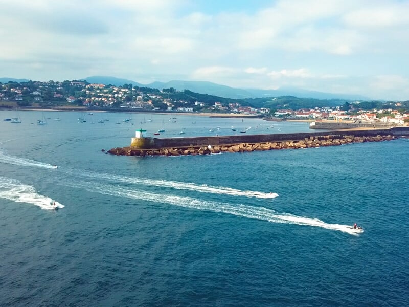 Vue aérienne de plusieurs jetskis naviguant sur une large étendue d'eau bleue avec une ville en arrière-plan.