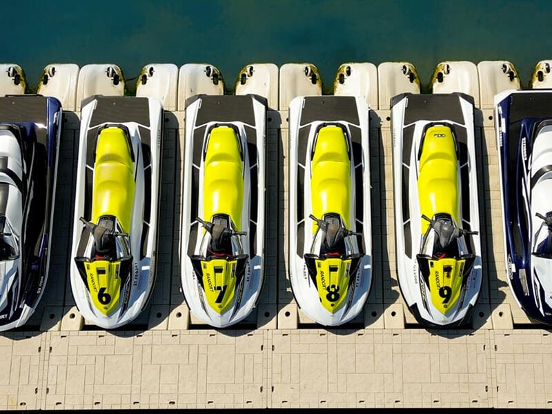 Vue aérienne de plusieurs jet skis jaunes et blancs alignés sur un ponton flottant, prêts pour la location ou une excursion.