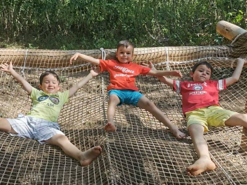 Trois enfants souriants allongés sur un filet suspendu en plein air.