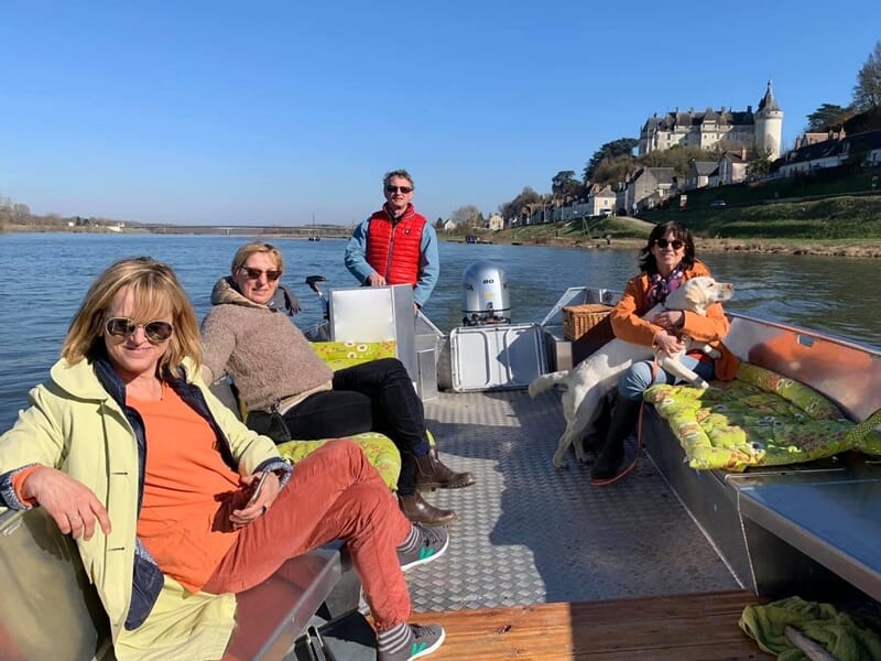Quatre personnes souriantes dans un bateau sur une rivière, avec un château visible en arrière-plan sous un ciel bleu.