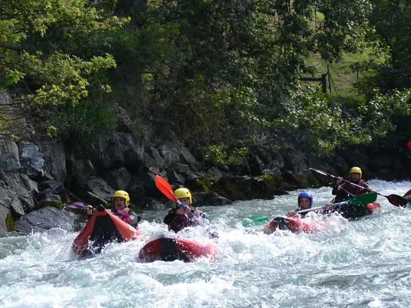 Groupe de personnes en rafting sur une rivière agitée, pagayant ensemble avec des casques jaunes et gilets rouges.
