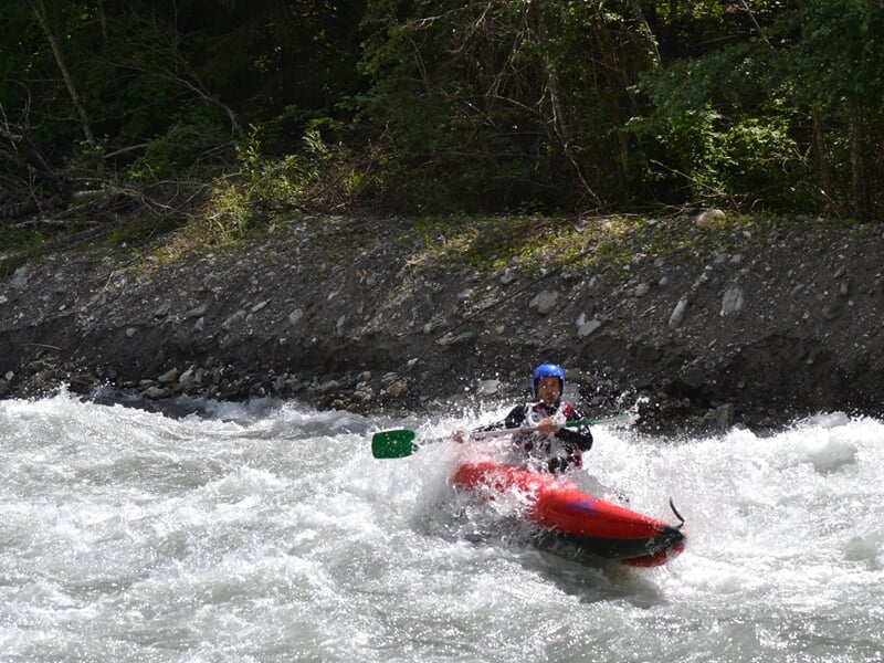 Rafting en rivière avec un seul pagayeur portant un casque bleu et un gilet de sauvetage rouge.