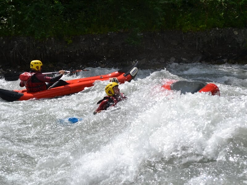 Deux kayakistes en kayak rouge pagayant vigoureusement dans une rivière à courant rapide.