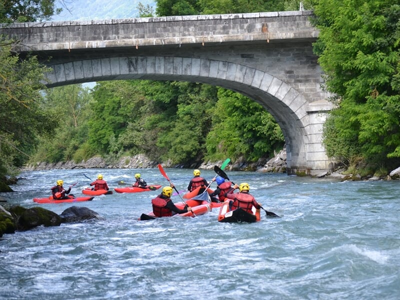 Trois kayakistes en kayak rouge naviguent dans des rapides avec des casques jaunes et gilets rouges.