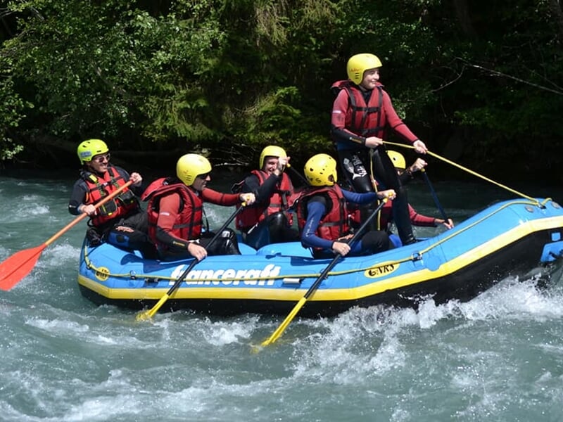 Groupe de kayakistes en kayak rouge pagayant dans une rivière sous un pont en béton.