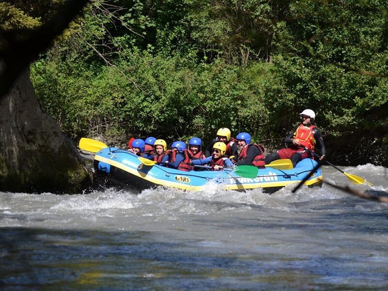 Groupe de huit personnes en rafting bleu affrontant des rapides avec enthousiasme et énergie.