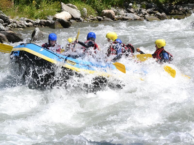 Rafting en rivière avec plusieurs personnes pagayant sous un pont, entouré d'arbres verts.
