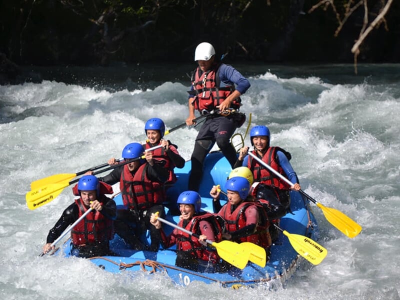 Rafting en rivière avec un groupe pagayant dans un bateau bleu sur une eau agitée.