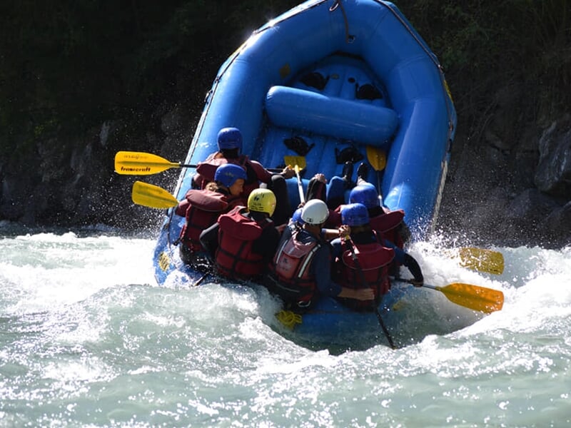 Rafting en rivière avec un groupe pagayant dans un bateau bleu, éclaboussures d'eau autour.