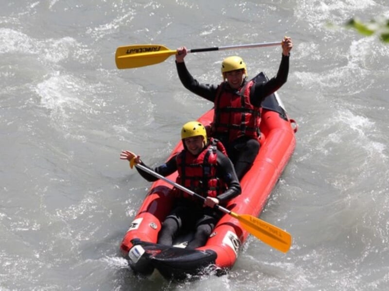 Deux kayakistes en kayak rouge pagayant dans une rivière à courant rapide entourée de rochers.