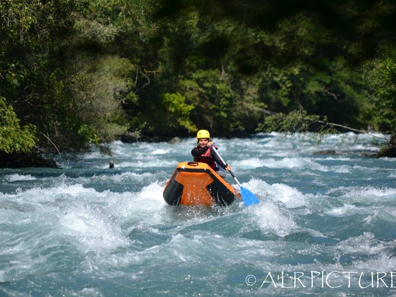 Trois kayakistes en kayak rouge pagayant dans une rivière agitée avec des casques jaunes.