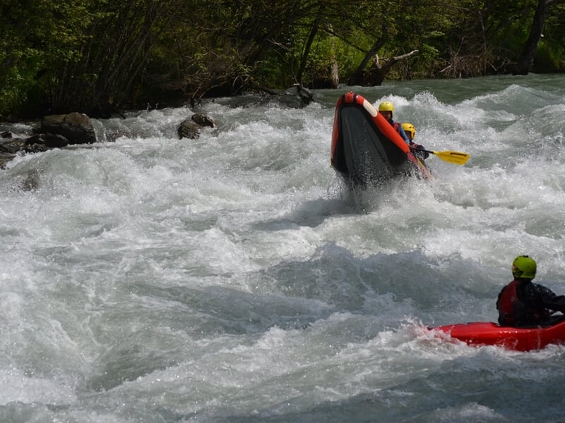 Quatre kayakistes en kayak rouge pagayant dans une rivière avec des rapides et des rochers.