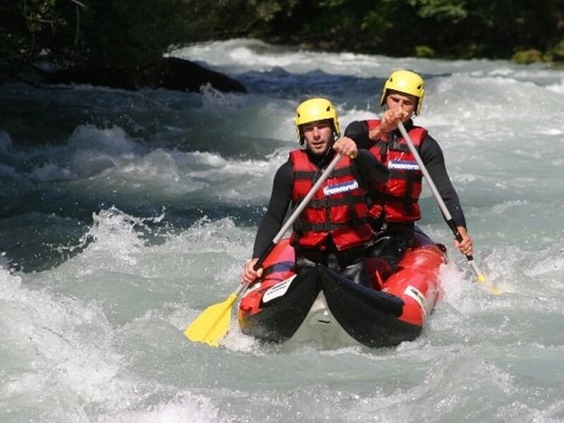 Kayakiste seul en kayak rouge pagayant dans une rivière agitée avec des rochers et des arbres.
