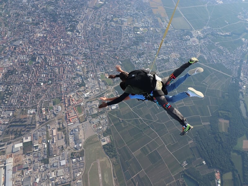 Vue aérienne de deux parachutistes en chute libre au-dessus d'une ville et de champs verts.