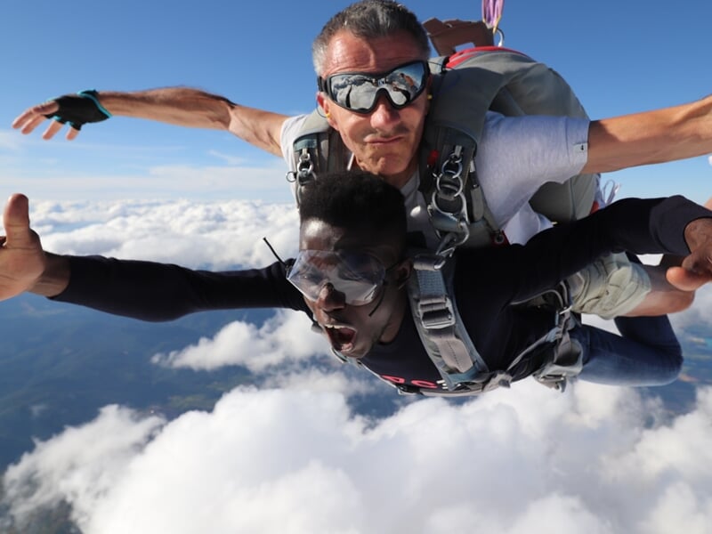 Deux parachutistes en tandem en chute libre, l'instructeur portant des lunettes de soleil.