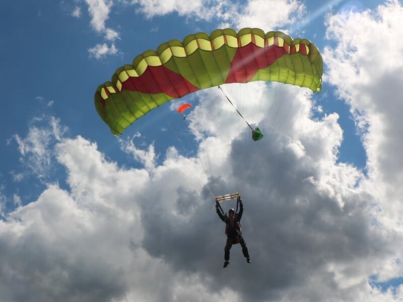 Parachutiste en chute libre avec un instructeur, tous deux souriants au-dessus des nuages.