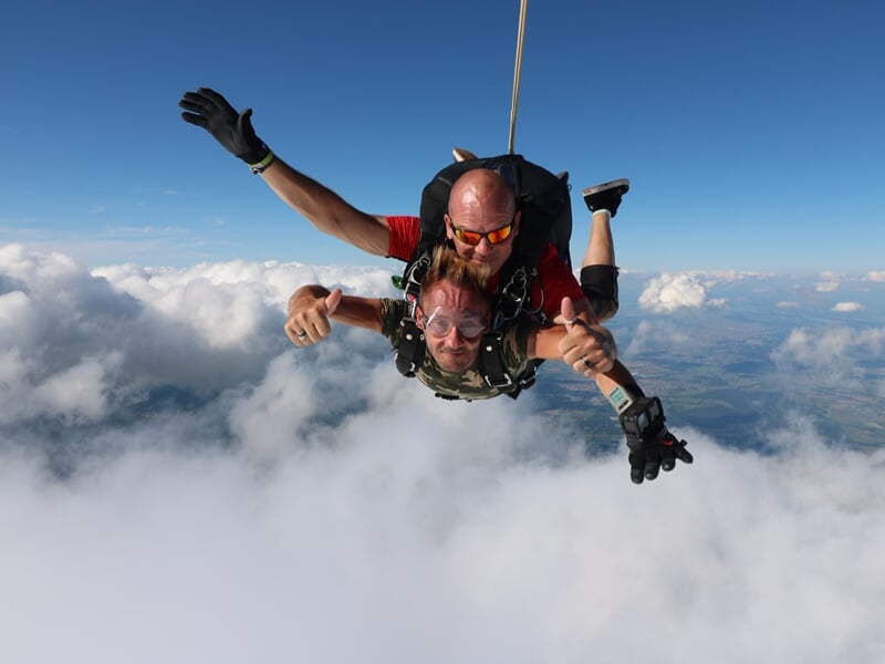 Jeune femme souriante assise dans un avion avant un saut en parachute, entourée d'autres passagers.