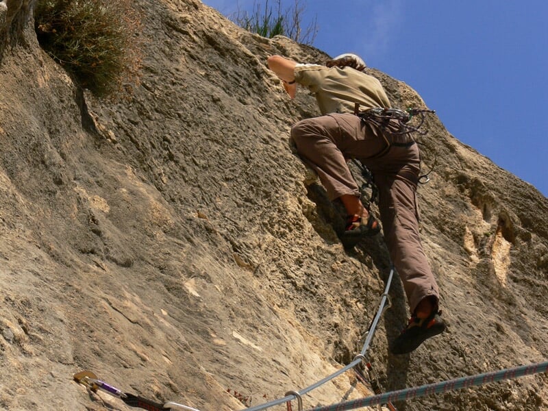 Un grimpeur en pleine ascension sur une paroi rocheuse inclinée, utilisant des prises naturelles dans la roche pour avancer.