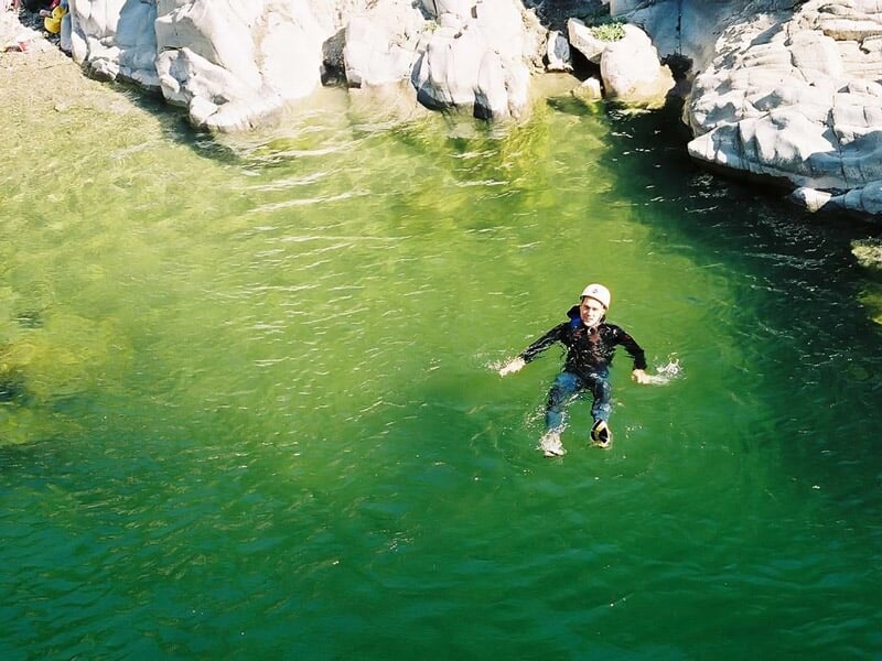 Personne flottant dans une eau claire entourée de rochers, portant un casque et une combinaison de canyoning.