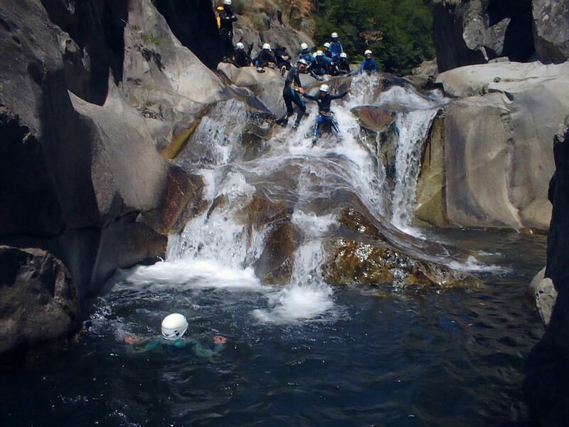 Groupe de personnes en casque sautant dans une piscine naturelle au pied d'une cascade rocheuse en canyoning.