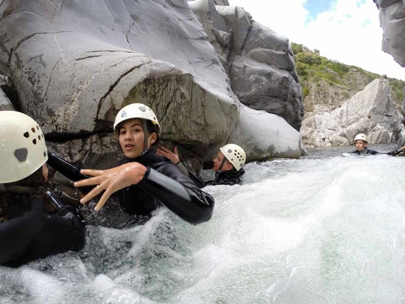 Participants en combinaison et casque progressant dans un courant d'eau vive entre des rochers lors d'une activité canyoning.