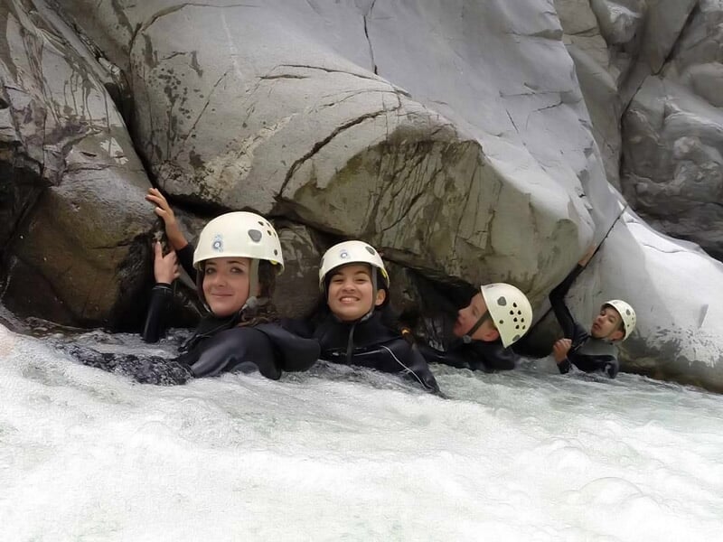 Quatre personnes souriantes en combinaison et casque tenant les rochers dans un courant d'eau vive en canyoning.