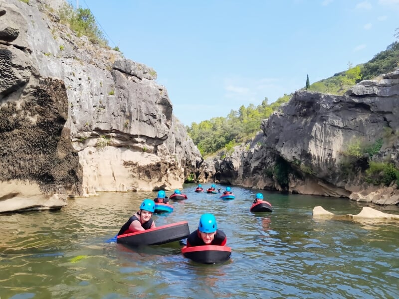 Groupe de personnes en casque bleu et combinaison nageant avec des flotteurs dans une rivière calme entourée de falaises.