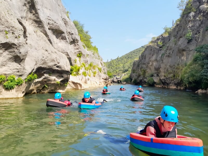 Plusieurs participants en casque bleu et combinaison nageant avec des flotteurs dans une rivière encaissée entre des falaises.