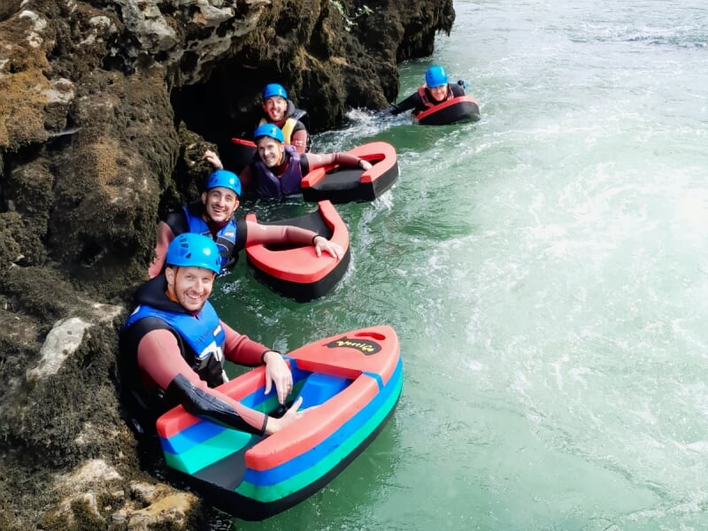Groupe souriant en casque bleu et combinaison assis sur des flotteurs colorés dans une rivière à l'eau claire.