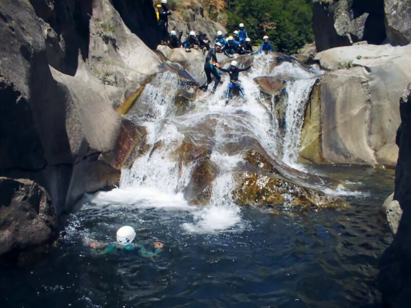 Groupe de personnes en casque sautant dans une piscine naturelle au pied d'une cascade rocheuse en canyoning.