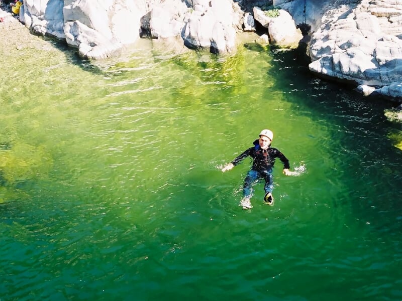 Personne flottant dans une eau claire entourée de rochers, portant un casque et une combinaison de canyoning.