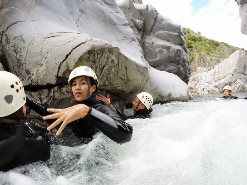 Participants en combinaison et casque progressant dans un courant d'eau vive entre des rochers lors d'une activité canyoning.