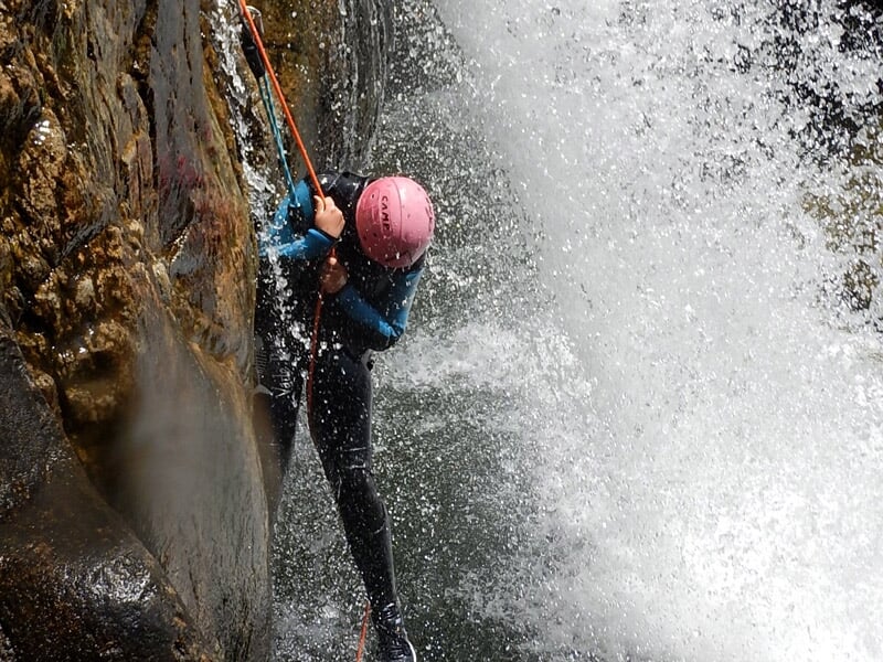 Personne pratiquant le canyoning sous une cascade