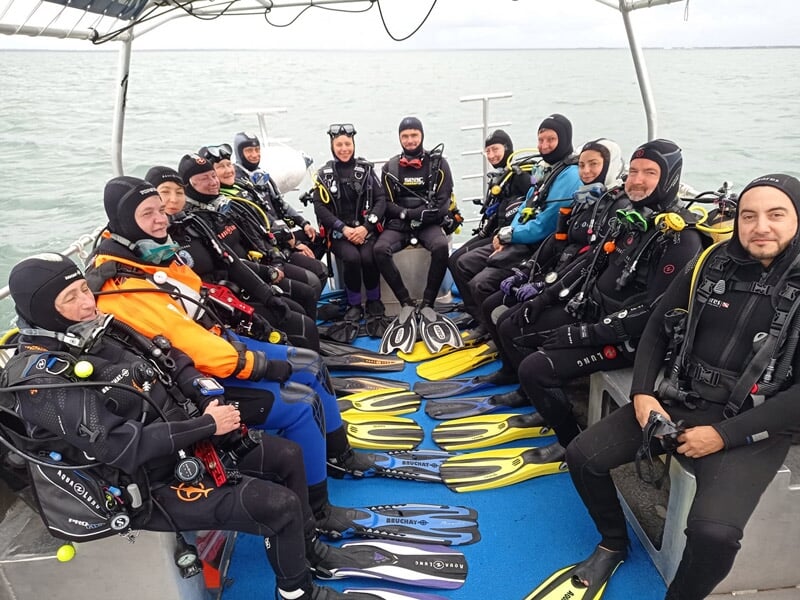 Groupe de plongeurs en combinaison complète assis sur un bateau prêts pour une plongée à Arcachon.