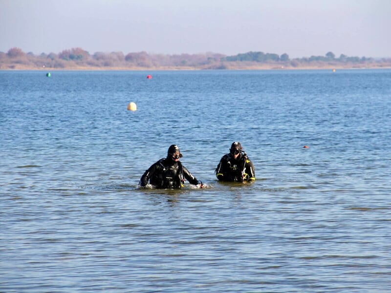 Deux plongeurs en combinaison noire marchant dans l'eau calme d'un plan d'eau à Arcachon.