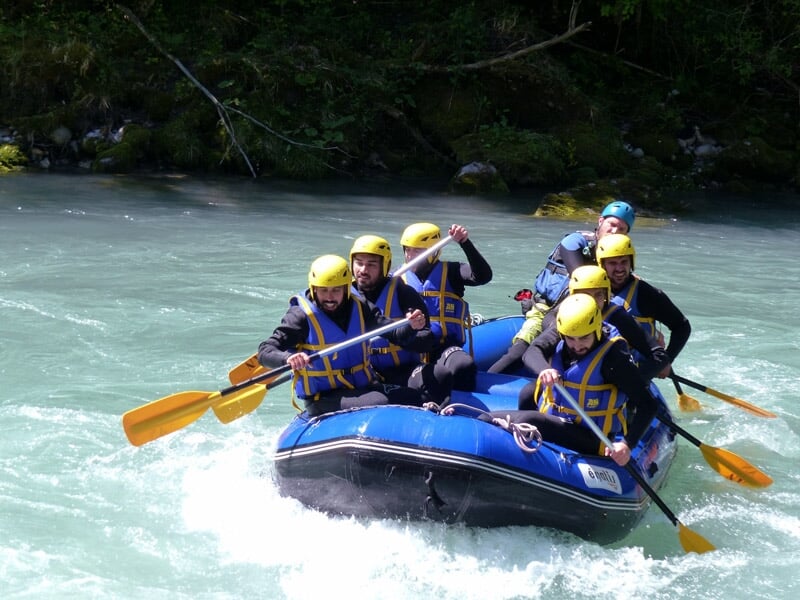 Un groupe de six personnes en raft bleu pagaient dans une rivière avec des rapides et rochers.