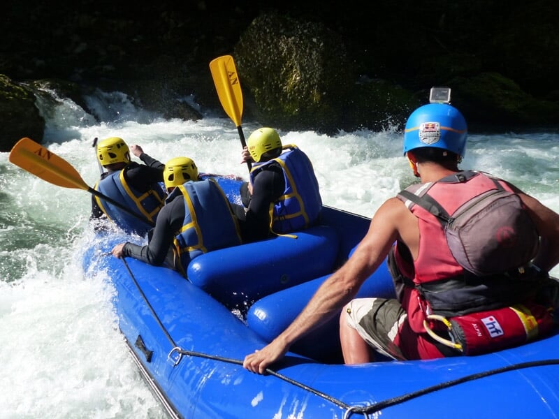 Un groupe de six personnes en raft gris pagaient dans une rivière entourée de végétation dense.