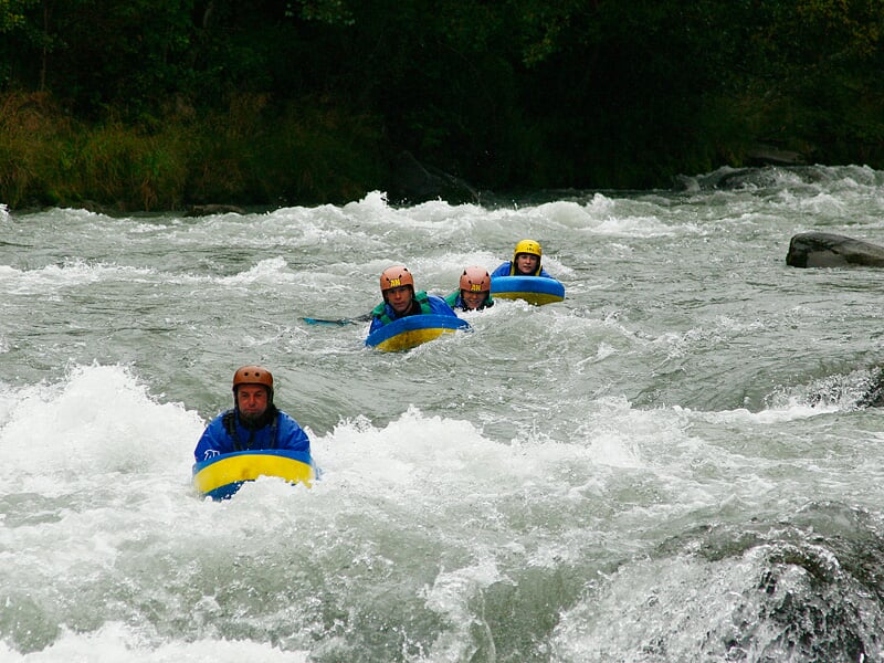 Trois personnes en hydrospeed descendent une rivière agitée avec des vagues et des rapides en pleine nature.