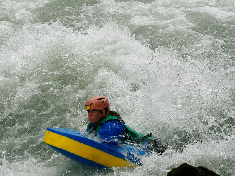 Un homme en hydrospeed navigue dans une eau vive avec de grosses vagues et éclaboussures autour de lui.