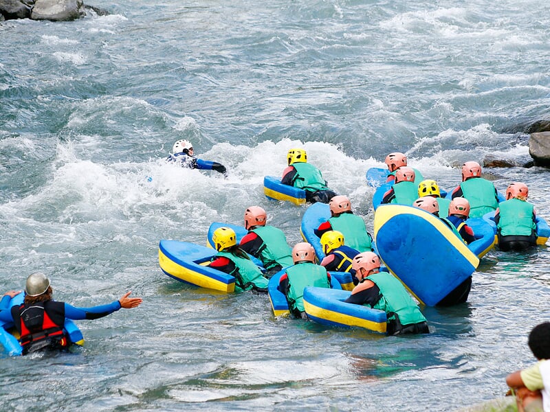 Plusieurs personnes en hydrospeed s'élancent dans une rivière agitée sous la surveillance d'un guide.