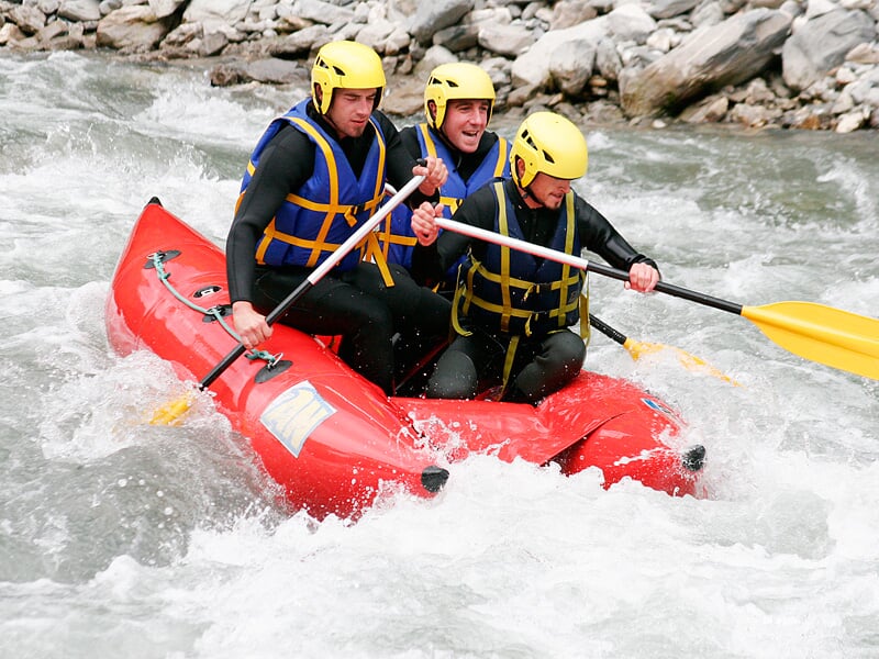 Trois hommes pagaient dans un raft rouge sur une rivière avec des rapides et éclaboussures d'eau.