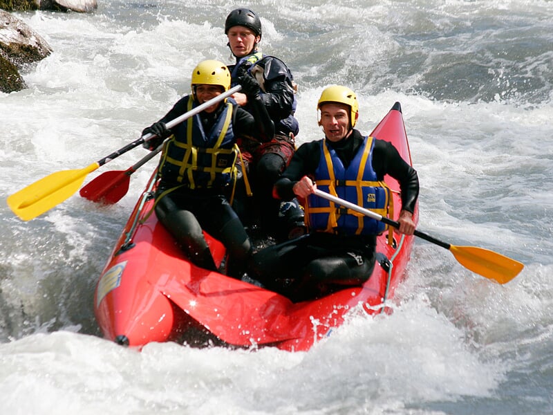 Trois personnes en raft rouge pagaient ensemble dans une rivière agitée avec des rochers visibles.